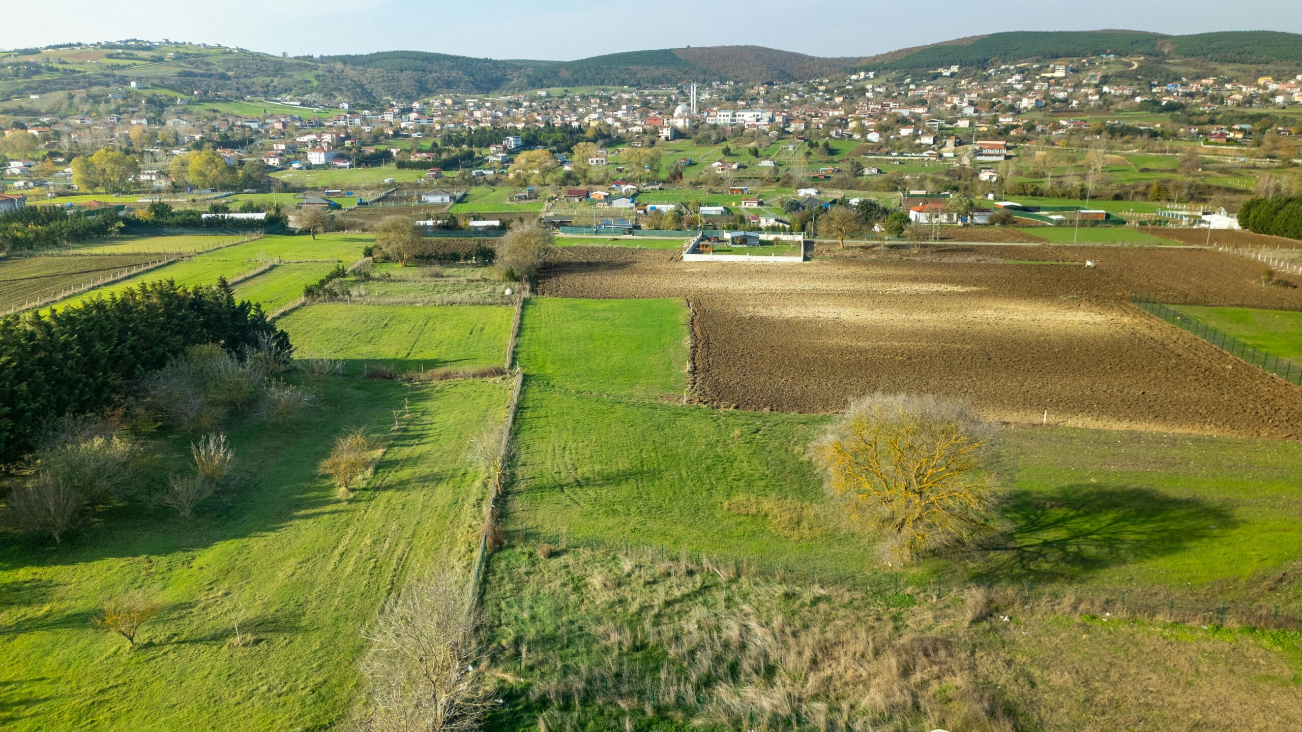 A propos de nous/ Zintyko homes Aerial shot showcasing lush green fields and quaint Turkish village in spring.