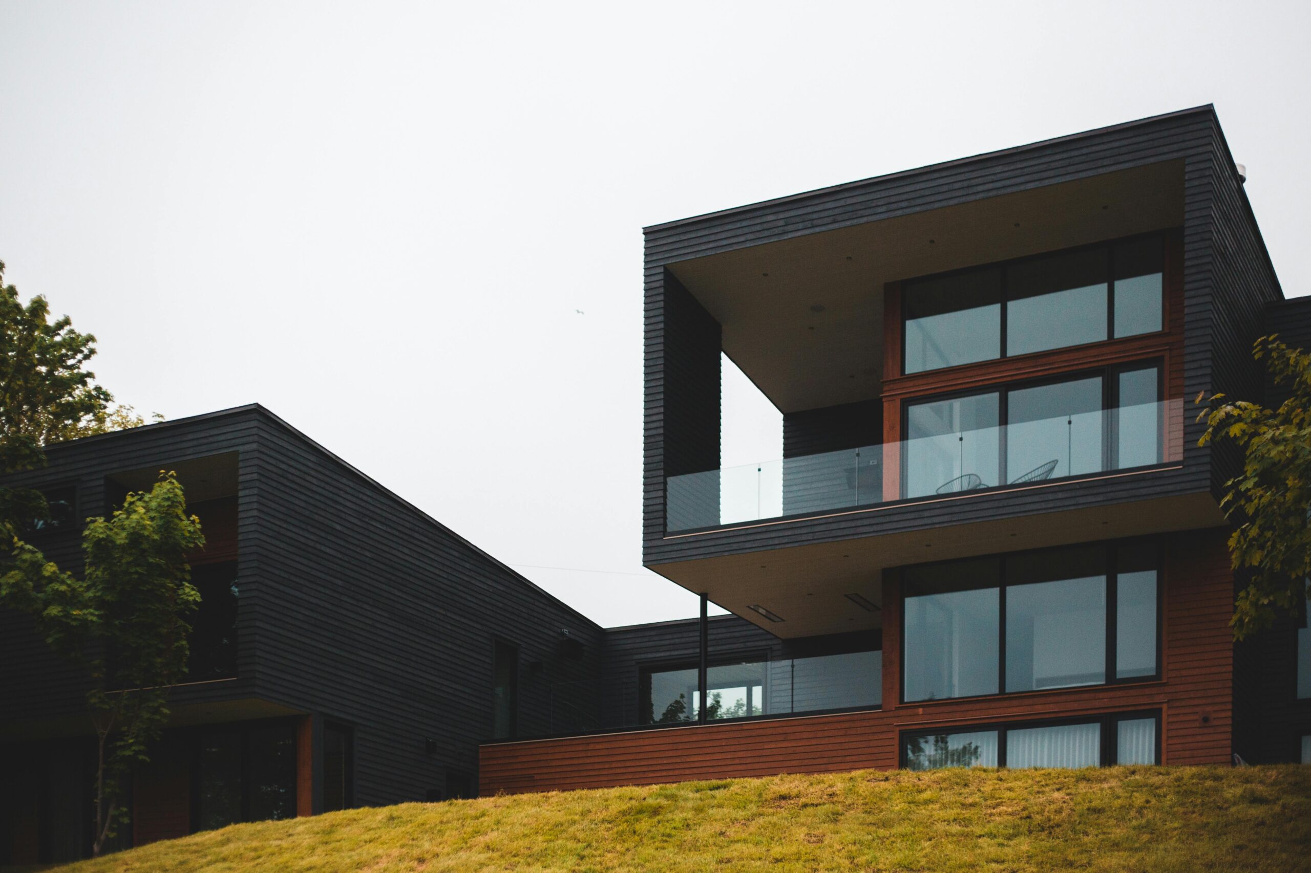 From below of contemporary geometric building with big windows and stylish design of balcony on green grass with trees